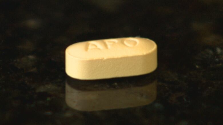 A yellow pill with the letters APO sits on a black surface.