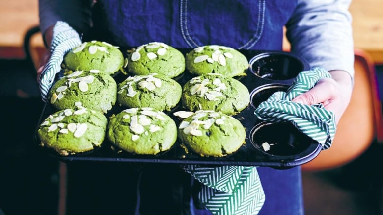 Closeup on hands holding a muffin tray of green tea muffins. 