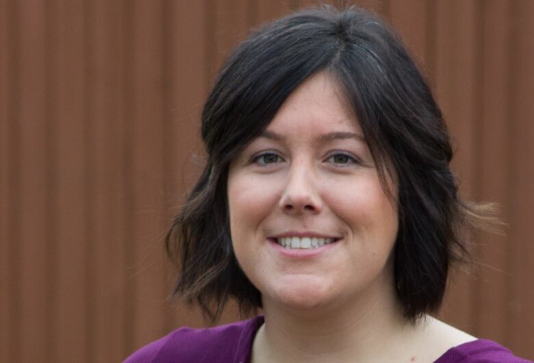 A smiling woman with brown hair is dressed in a purple shirt.