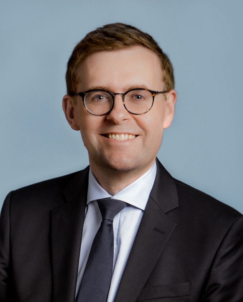 A man wearing a suit with glasses smiles.