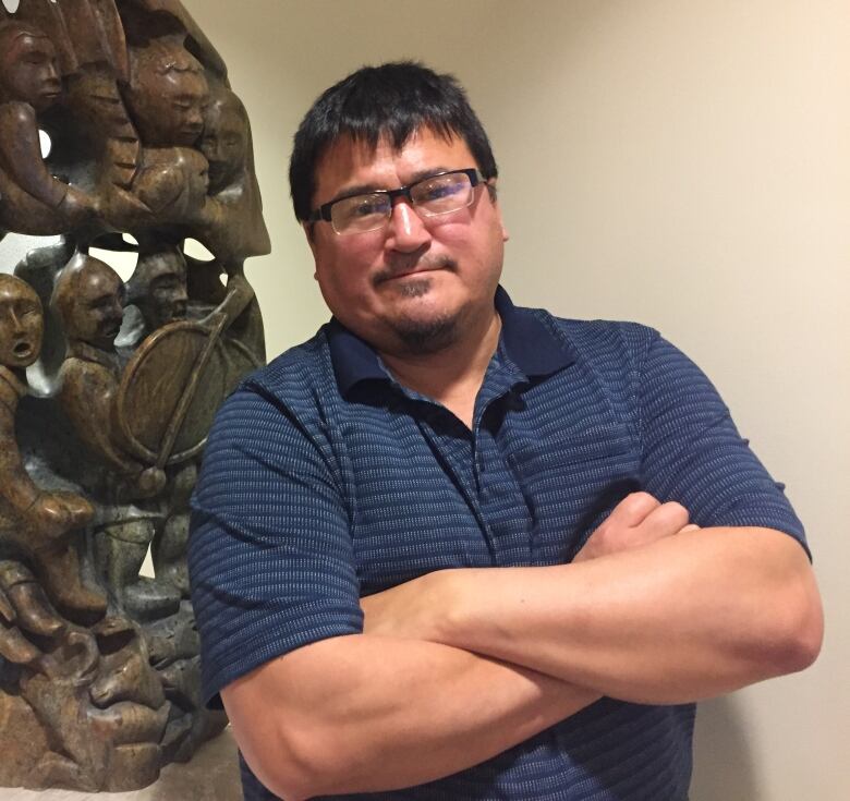 A man in glasses poses in front of a large sculpture inside a building.