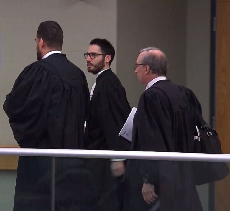 Three men in legal robes walk together in a courthouse interior.