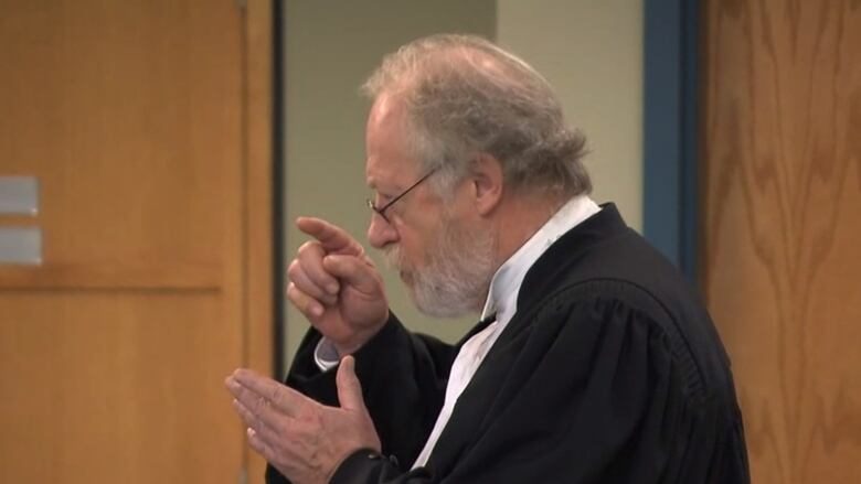 Man in black and white legal robes gestures.