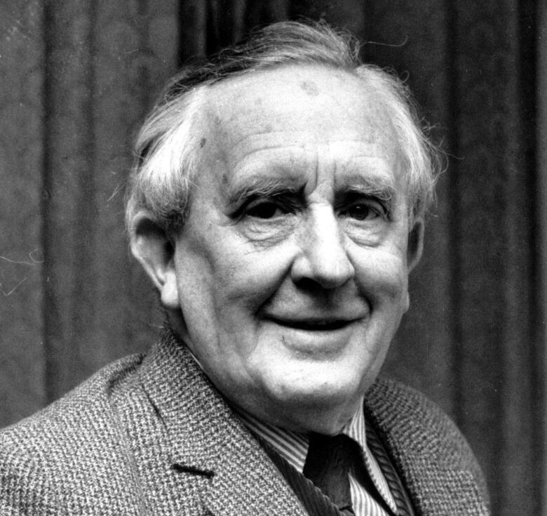 A man wearing a suit with greying hair smiles at the camera. The photo is in black and white. 