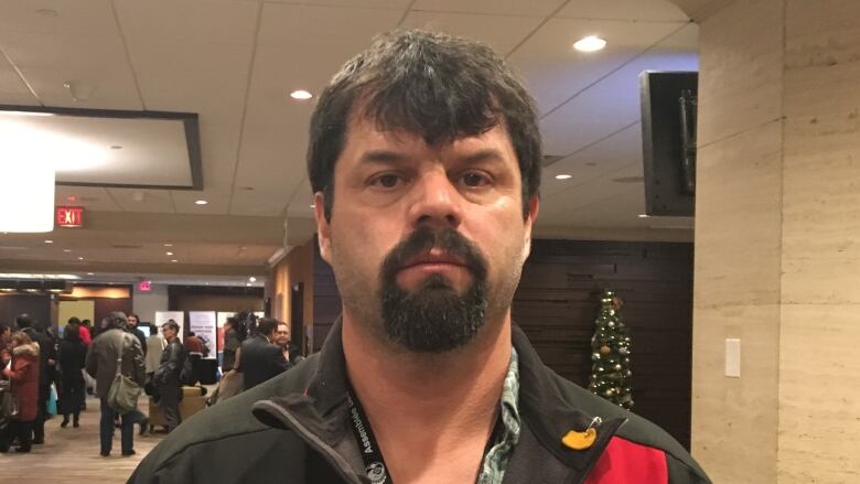 A man with beard stands in front of a crowd.