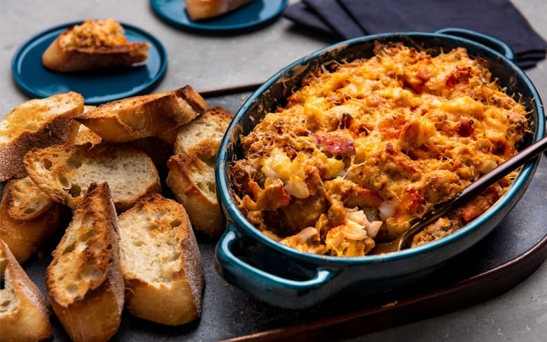 Baked lobster dip in a blue serving dish with slices of baguette next to the dip. 