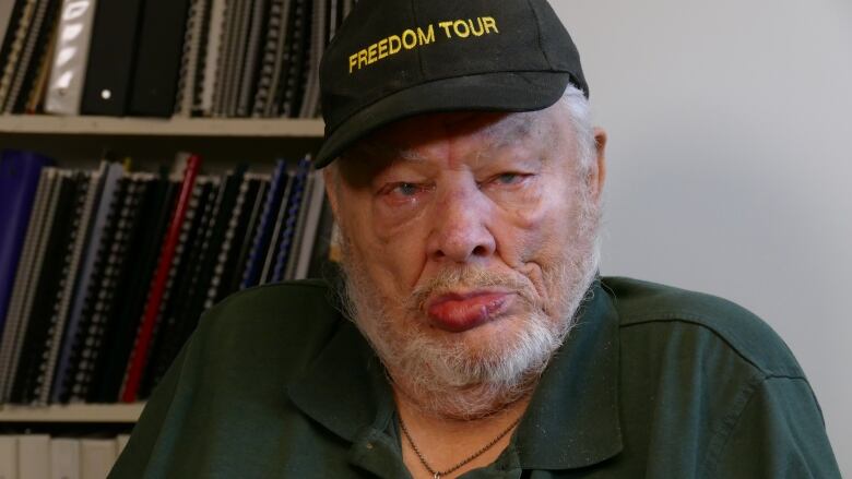 Old man with grey beard, wearing a ball cap.