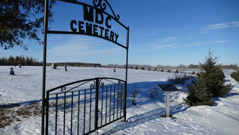 Wrought-iron gate in front of a cemetery reads 'MDC CEMETERY.'