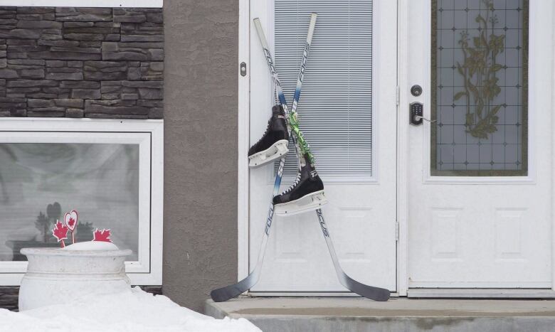 A pair of hockey sticks are set on a front door in 2018. They are crossed and a pair of skates hangs from them. 