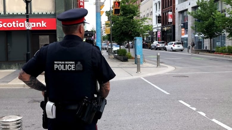 A uniformed police officer stands on a street corner in a downtown area