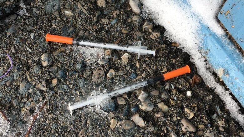 Two needles with orange tops lie on a ground in the winter. 