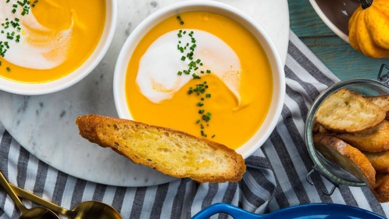 Overhead shot of bowls of creamy orange soup with a small toast on top of one. 