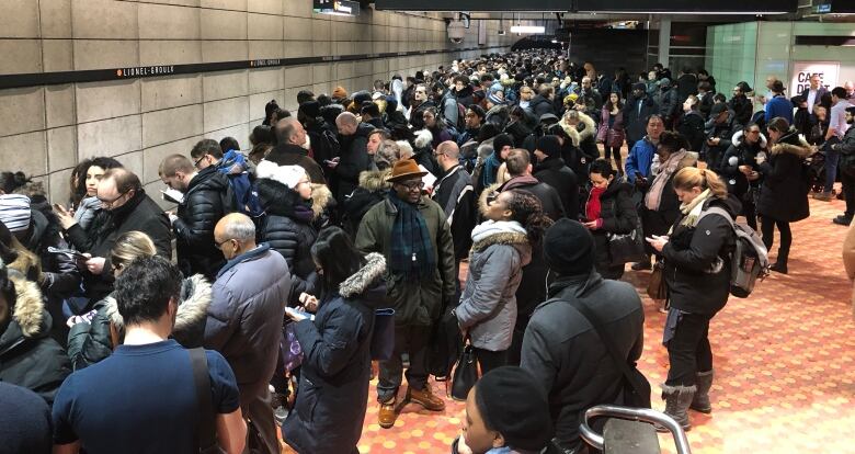 A crowd of frustrated-looking people stand on the Metro platform.