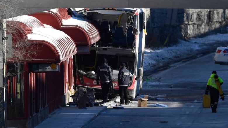 Two men in black jackets look at a damaged bus. 