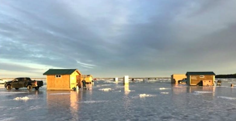 Wooden ice fishing huts sit upon a frozen lake on a sunny day