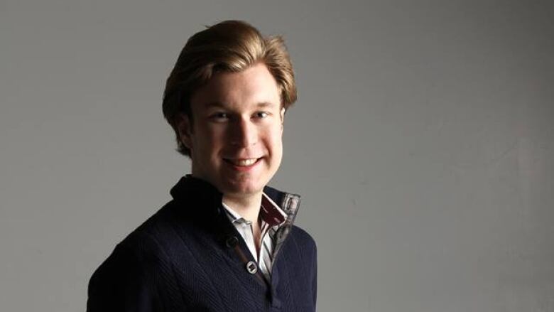 A young man wearing a sweater smiles at the camera.