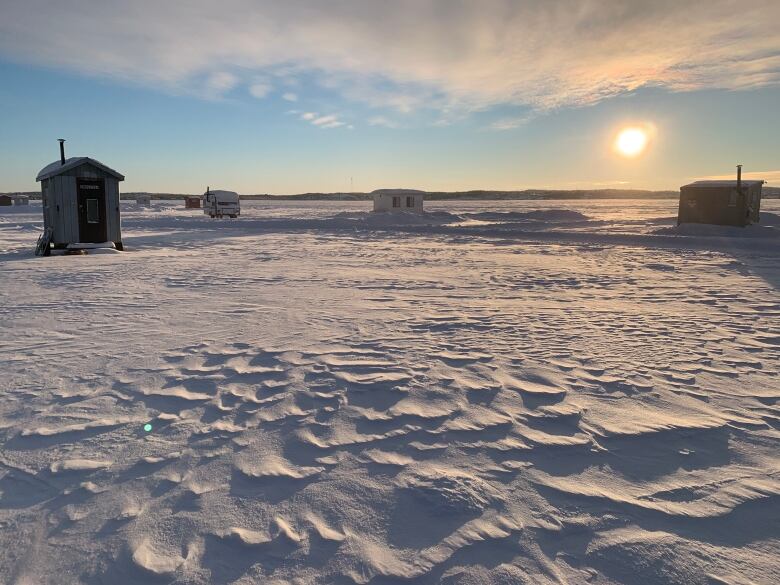 a few huts scattered over a frozen snowy lake with a sunset glowing in the background