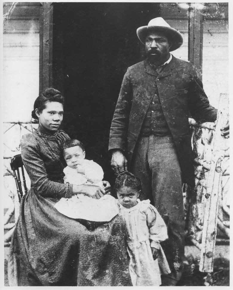 A man is seen posing in an old black and white photograph with his wife and two kids.