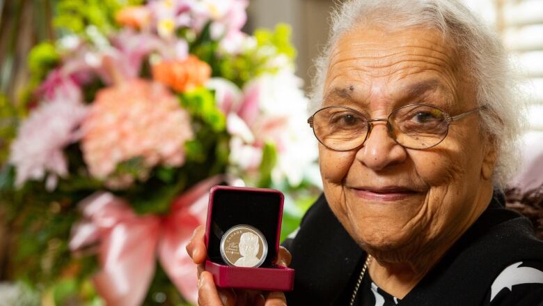 An older Black woman with white hair holding a coin