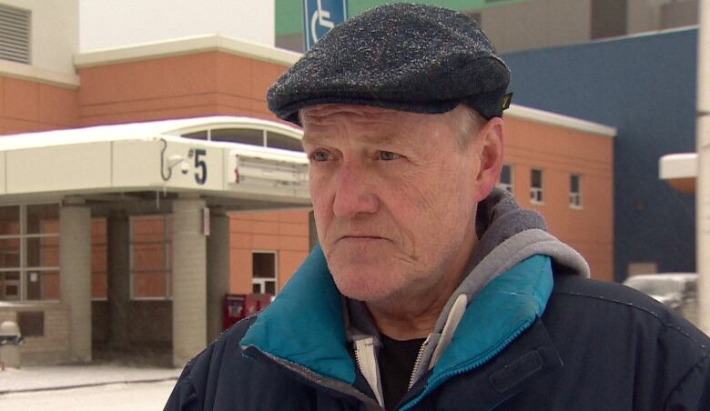 Yukon Employees Union President Steve Geick stands in front of the Whitehorse General Hospital with a black cap on. 