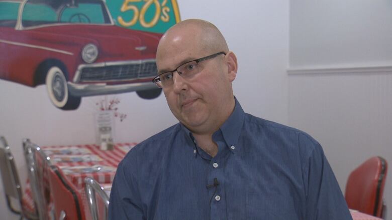 A bald man with glasses wearing a blue button-up shirt