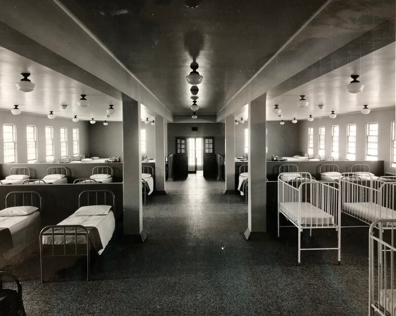 Black-and-white photo of a dormitory with beds on either side.