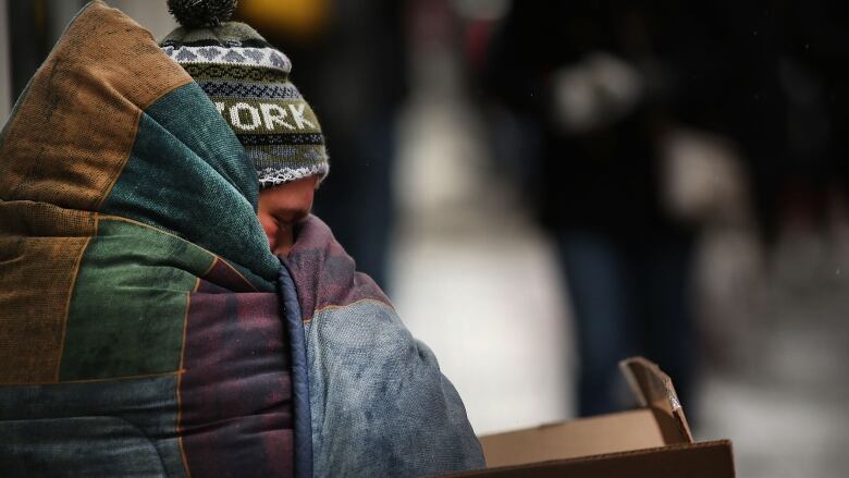 A person wrapped up in a blanket outside, with a toque on.