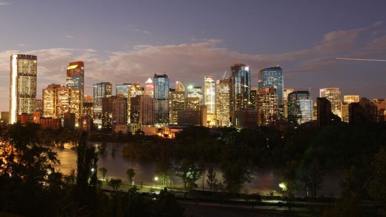 a view of calgary's skyline with a purple-blue sky behind it. the sun is setting