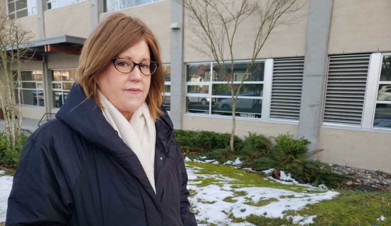 A white woman wearing a coat looks to the camera during a snowy day.