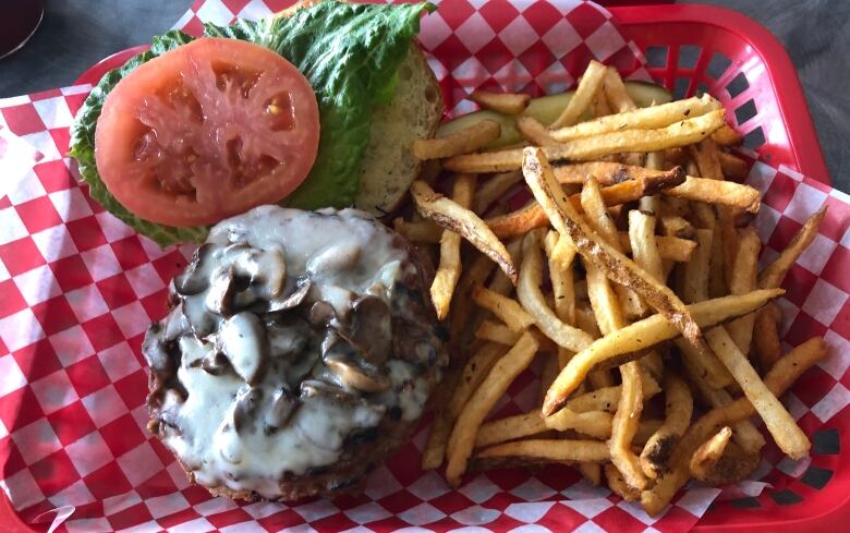 A burger smotheres in mushrooms and cheese sits open-face next to a pile of fries.