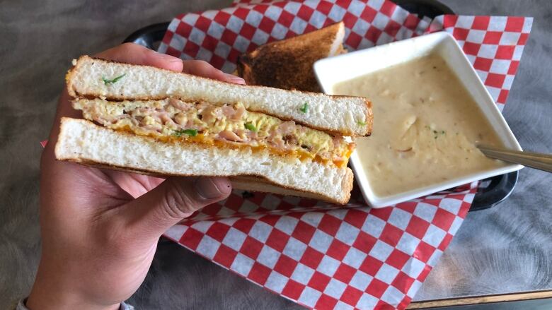 The cross-section of an egg and ham sandwich next to a bowl of creamy soup.