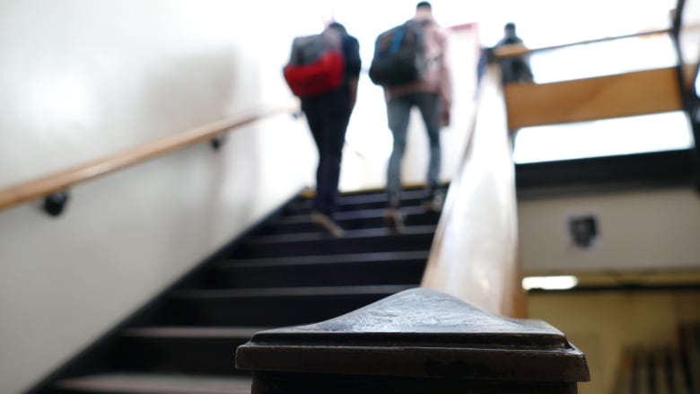 A blurred photo shows the backs of students wearing backpacks walking up a set of stairs in a school.