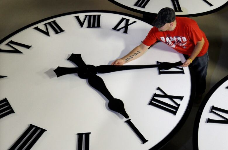 A man moves the hands of a gigantic clock.