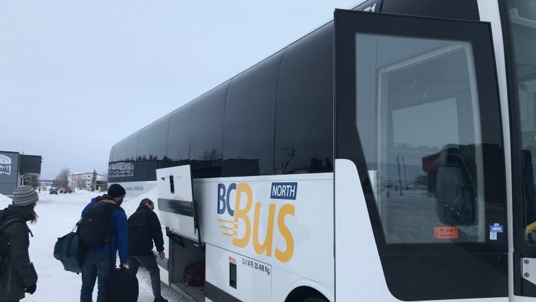 A group of people board a bus with the title 'BC Bus North' on a snowy road.