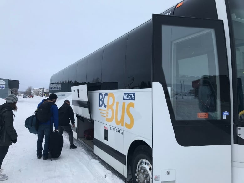 A group of people board a bus with the title 'B.C. Bus North' on a snowy road.