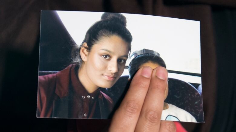 Woman's hand holds a photograph showing a teenage girl. Two fingers cover the face of a younger girl in the photo beside her.