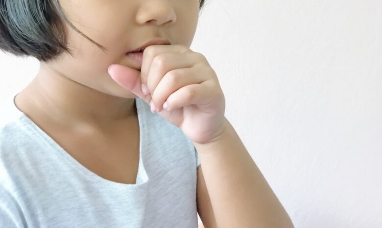 A child coughs while covering their mouth with their hand