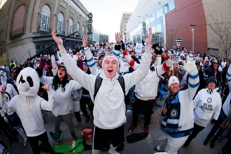  A crowd of hockey gans in white shirts and sweaters on a street outside Canada Life Centre.