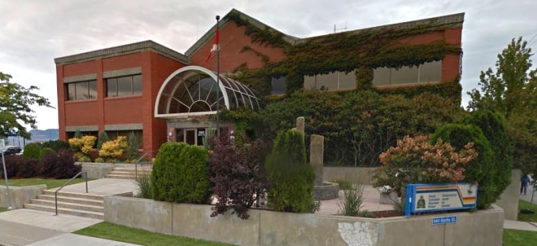 A long, red building with a peaked roof and an entrance arch with an RCMP sign outside.