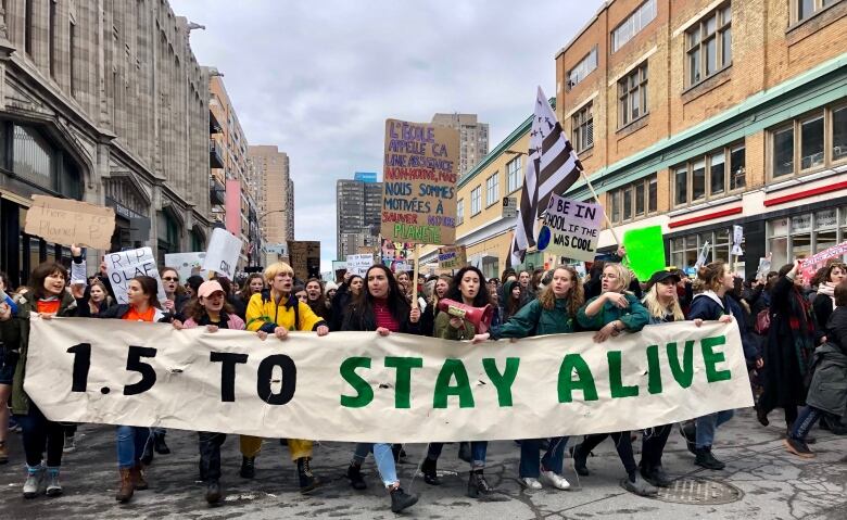 Students carrying a banner reading '1.5 to stay alive' march down a street in downtown Montreal.