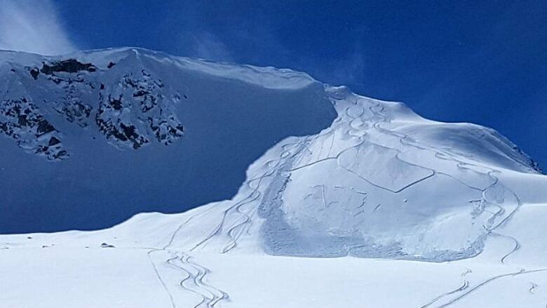 Lines running down snow covered mountains. The sky is clear blue.