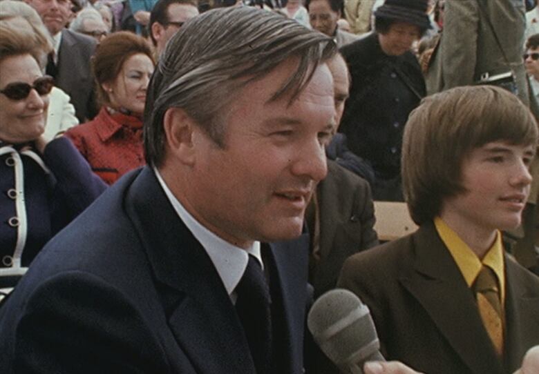 Man in 1970s clothing being interviewed with microphone held towards him