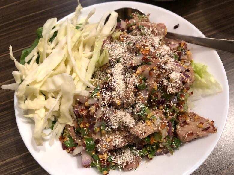 A pile of shredded meat on a plate covered in spices, sitting next to shredded cabbage.