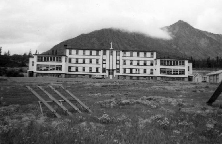 A black and white photo of a large school building with a mountain behind it.