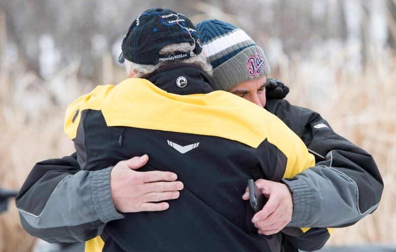 A man in a tuque embraces another man.