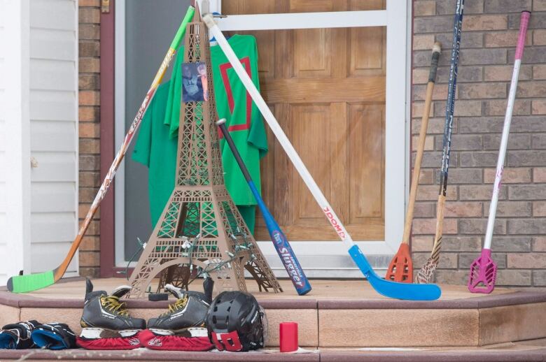 Hockey sticks and equipment lie propped up against a front porch. 