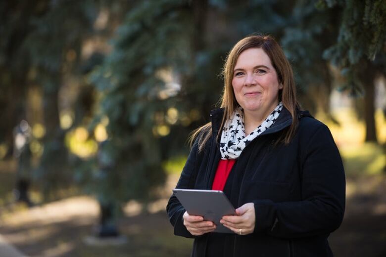 A woman stands outside holding an ipad. 