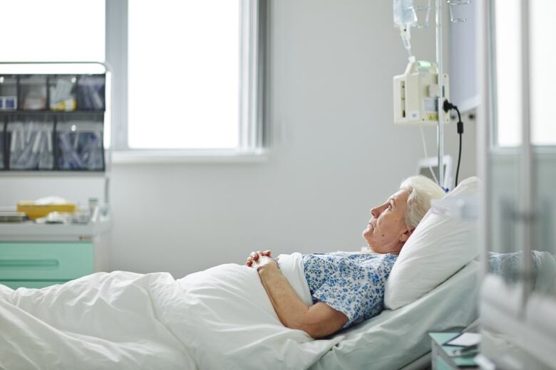 A woman with white hair in a hospital bed staring up.