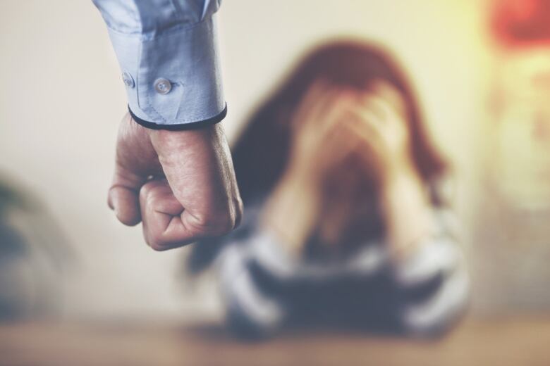 A blurred photo shows a closeup of a man's fist with a woman holding her head in her hands in the background.