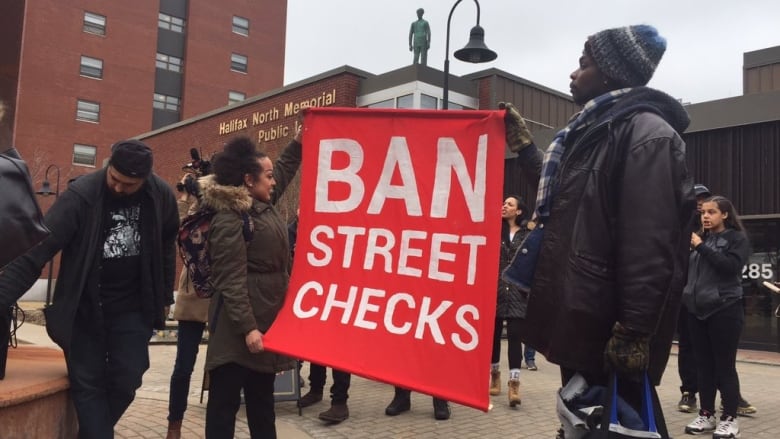 A group of people stand in front a library holding a sign that says 